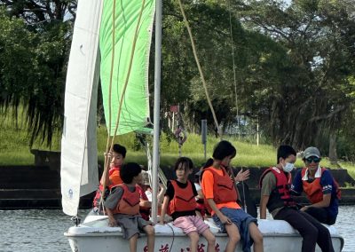 孩子們坐在帆船船頭,雙腳懸在冬山河水面上
